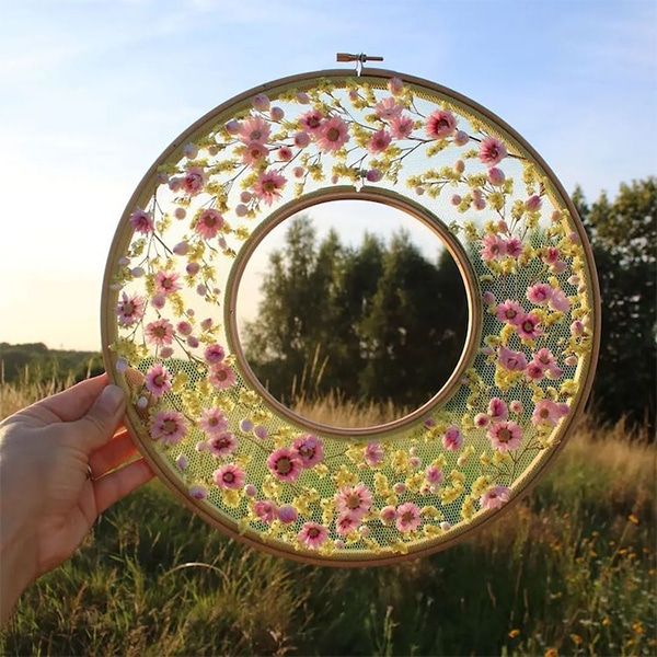 a hand holding a glass plate with flowers painted on it in front of a grassy field