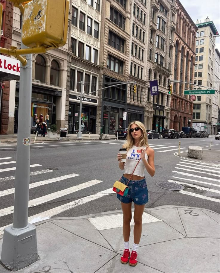 a woman is standing on the sidewalk drinking coffee