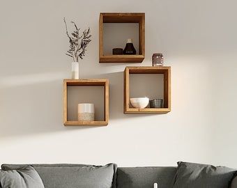 three square wooden shelves on the wall above a gray couch in a white living room