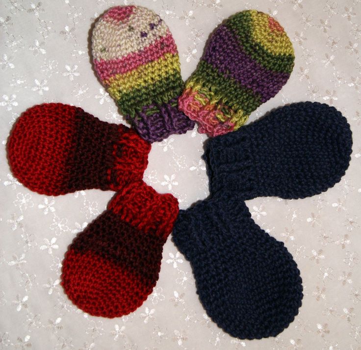 four knitted mittens arranged in a circle on top of a white tablecloth