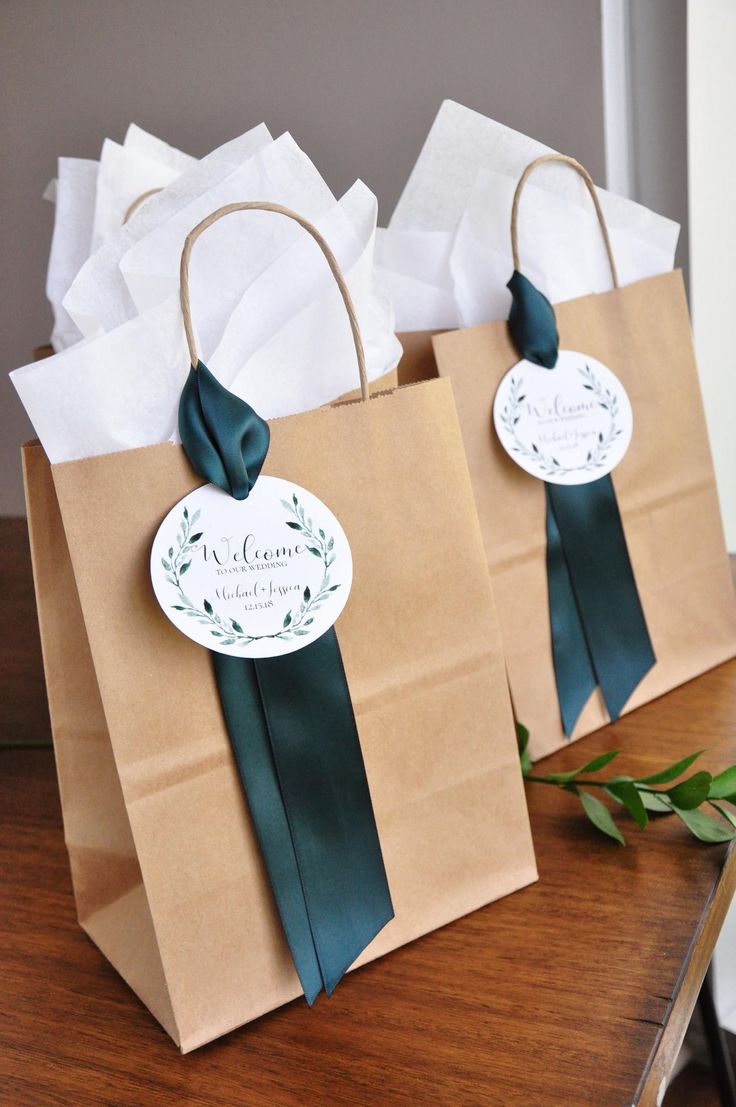 two brown paper bags with green ribbons and tags on them sitting on a wooden table