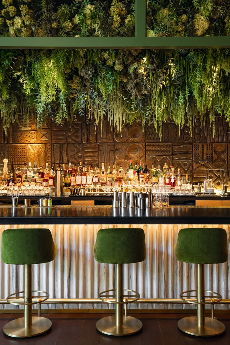 the bar is decorated with greenery and gold bars stools are lined up in front of it