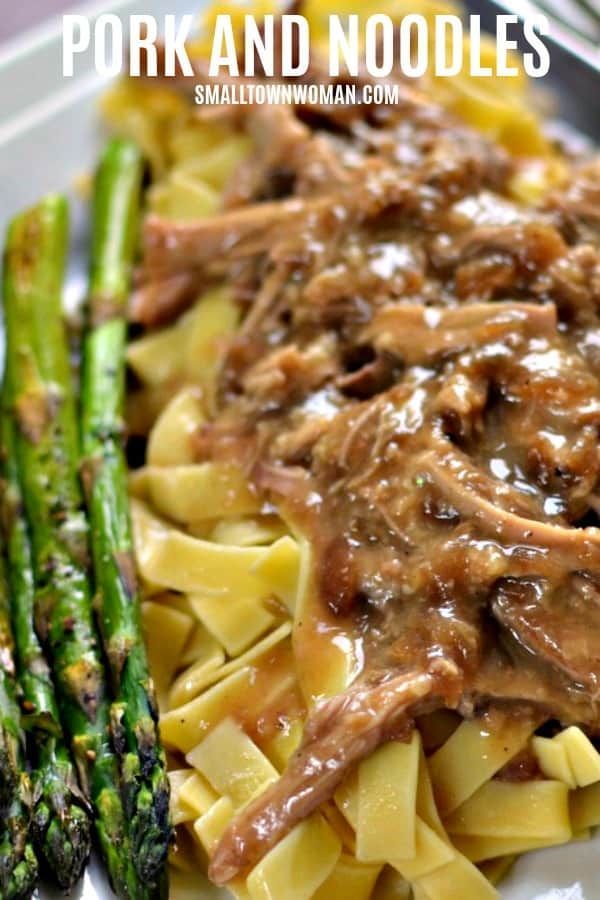 beef and noodles with gravy on a white plate next to asparagus