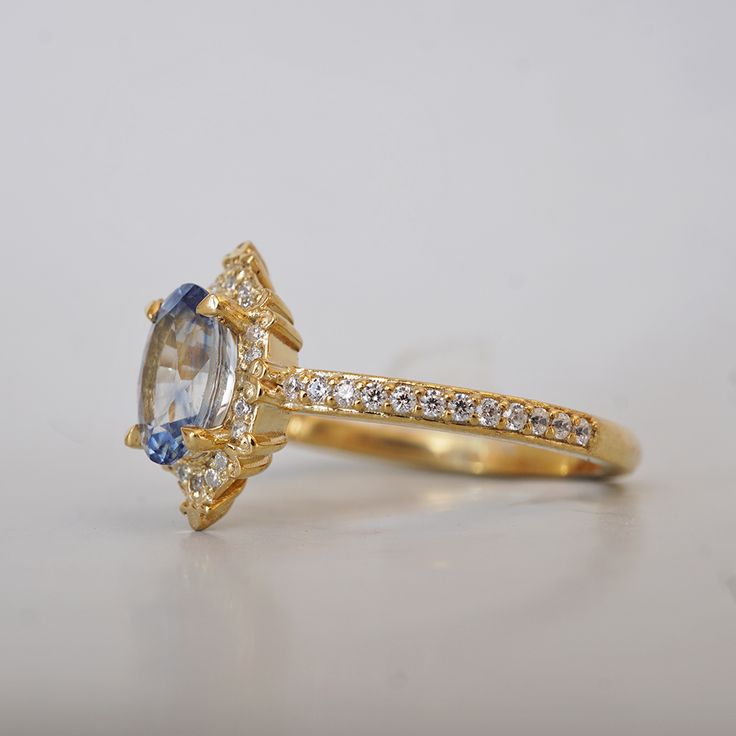 Introducing the Skybound Ring, a ring that embodies the serene beauty of the heavens with a touch of timeless elegance. At the heart of this exquisite piece lies a captivating oval-cut parti-color sapphire, its delicate blue hues reminiscent of a clear, boundless sky. The sapphire is encircled by a halo of brilliant diamonds, each one meticulously set in a vintage-inspired gold setting that adds a touch of classic sophistication. The delicate detailing on the band, paired with the radiant sparkle of the diamonds, creates a sense of effortless elegance. All orders come in our Tippy Taste ring box. This ring is handmade and designed in NYC. 14K or 18K solid gold Natural oval bi-color sapphire, 1.06ct 42 Natural round diamonds. SI clarity. GH color Total diamond carat weight, approx. 0.17ct 1 Gold Tanzanite Ring With Halo Setting, Elegant 14k Gold Cushion Cut Sapphire Ring, Yellow Gold Sapphire Ring With Halo Design, Elegant Yellow Gold Sapphire Ring With Halo, Oval Yellow Gold Halo Ring With Ethical Diamonds, Luxury Sapphire Oval Halo Ring, Luxury Oval Sapphire Halo Ring, Celestial Style Oval Diamond Promise Ring, Elegant Gold Sapphire Ring With Halo Design