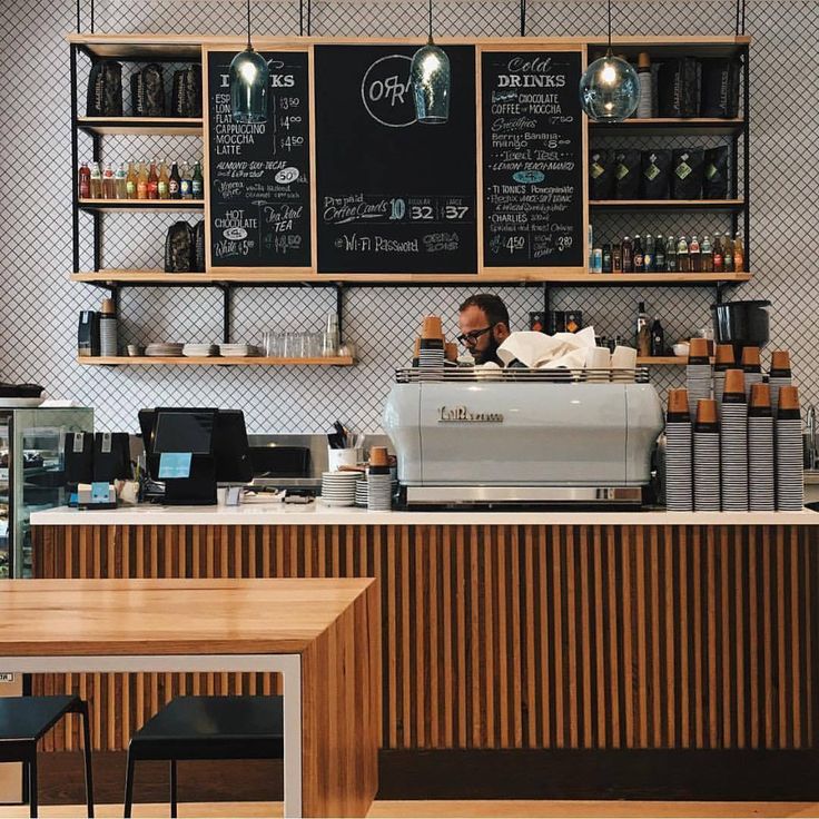 a man is behind the counter at a coffee shop with menus on the wall