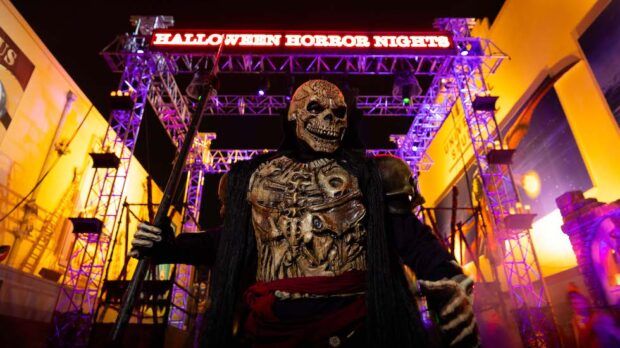 a man dressed up as a skeleton stands in front of a halloween horror nights sign