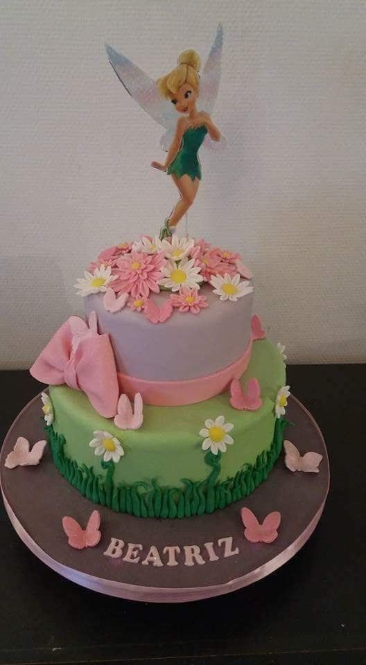 a birthday cake with a tinkerbell topper and flowers on the bottom tier