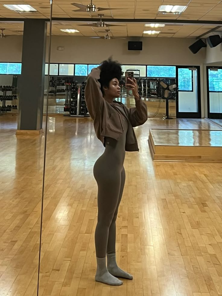 a woman taking a selfie in an empty gym with mirrors on the wall and hard wood flooring