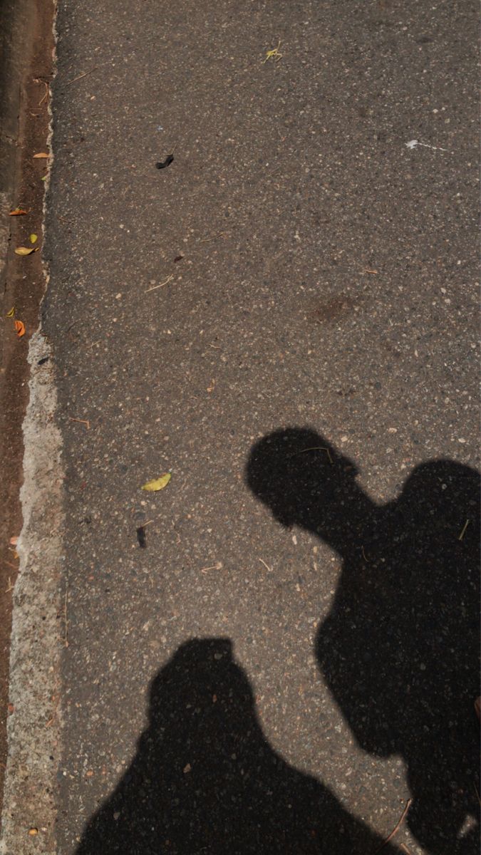 the shadow of a person riding a skateboard down a street next to a curb