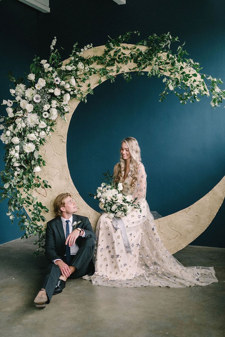 a man sitting next to a woman in front of a moon with flowers on it