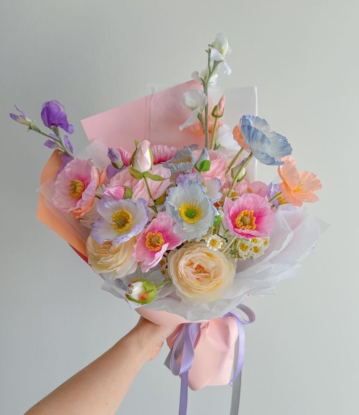 a bouquet of flowers is being held by a person with a pink ribbon around it