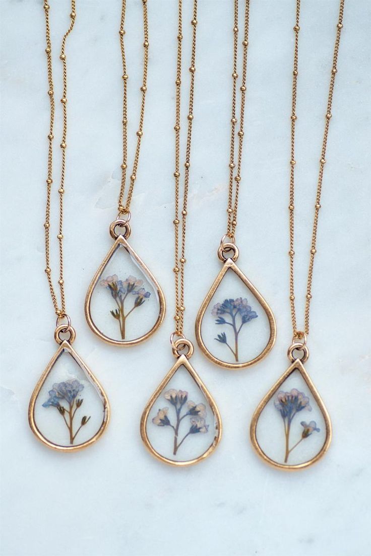 three necklaces with flowers in them on a marble surface, one is gold and the other is white