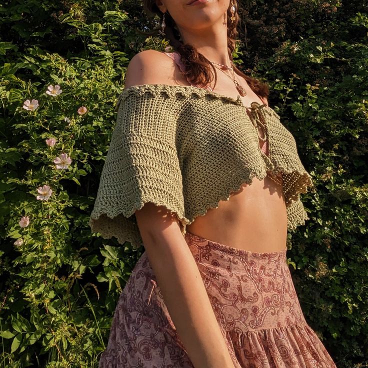 a woman wearing a crochet top and skirt standing in front of some bushes