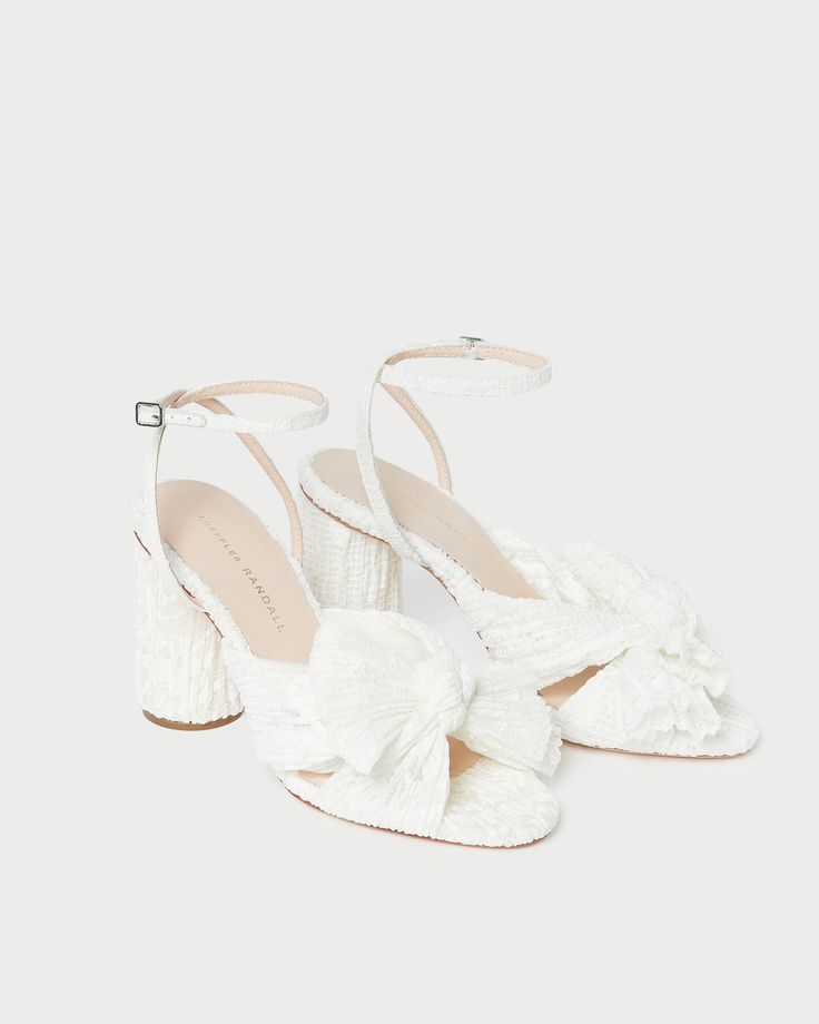 Pleated, heeled sandal in white fabric covered with cream lace and topped with our signature knotted bow. Features a padded footbed with gold stamped logo. Open toe with adjustable buckle ankle strap. 3.5 inch heel. Camellia White, Ethereal Garden, Flower Heels, Bow Sandals, Bow Heels, Cream Flowers, Wedding Heels, Heeled Sandal, Lace Bows