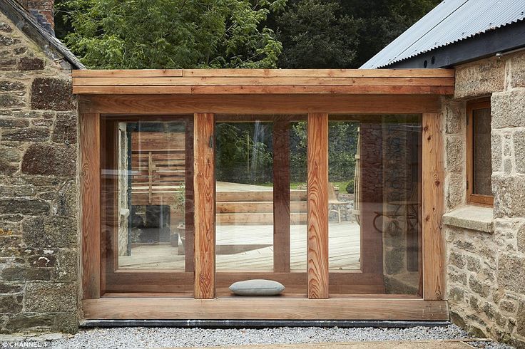 an open wooden door in front of a stone building with glass doors on both sides