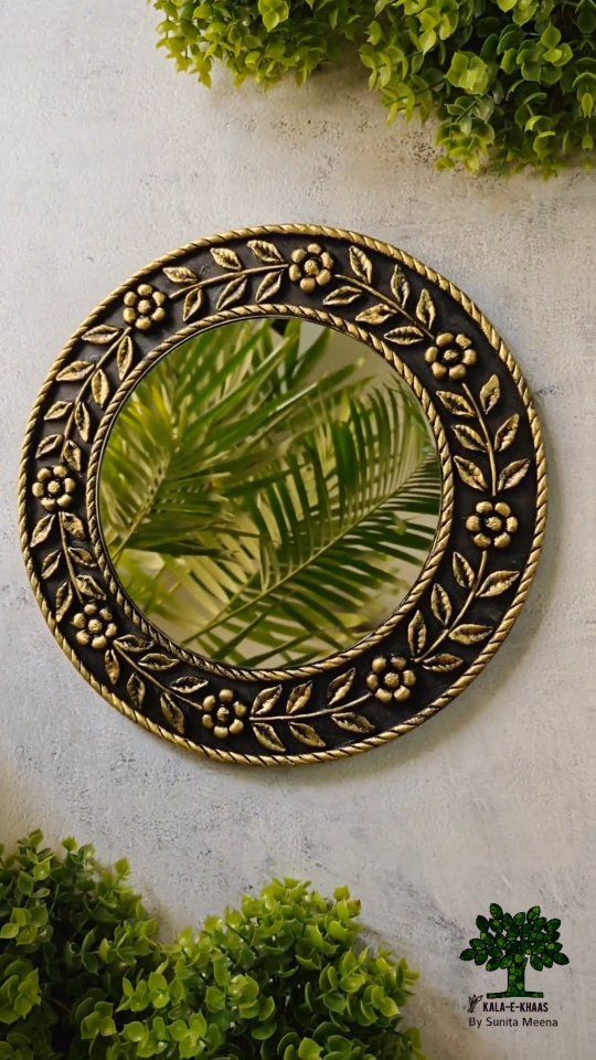 a round mirror hanging on the side of a wall next to some green plant life