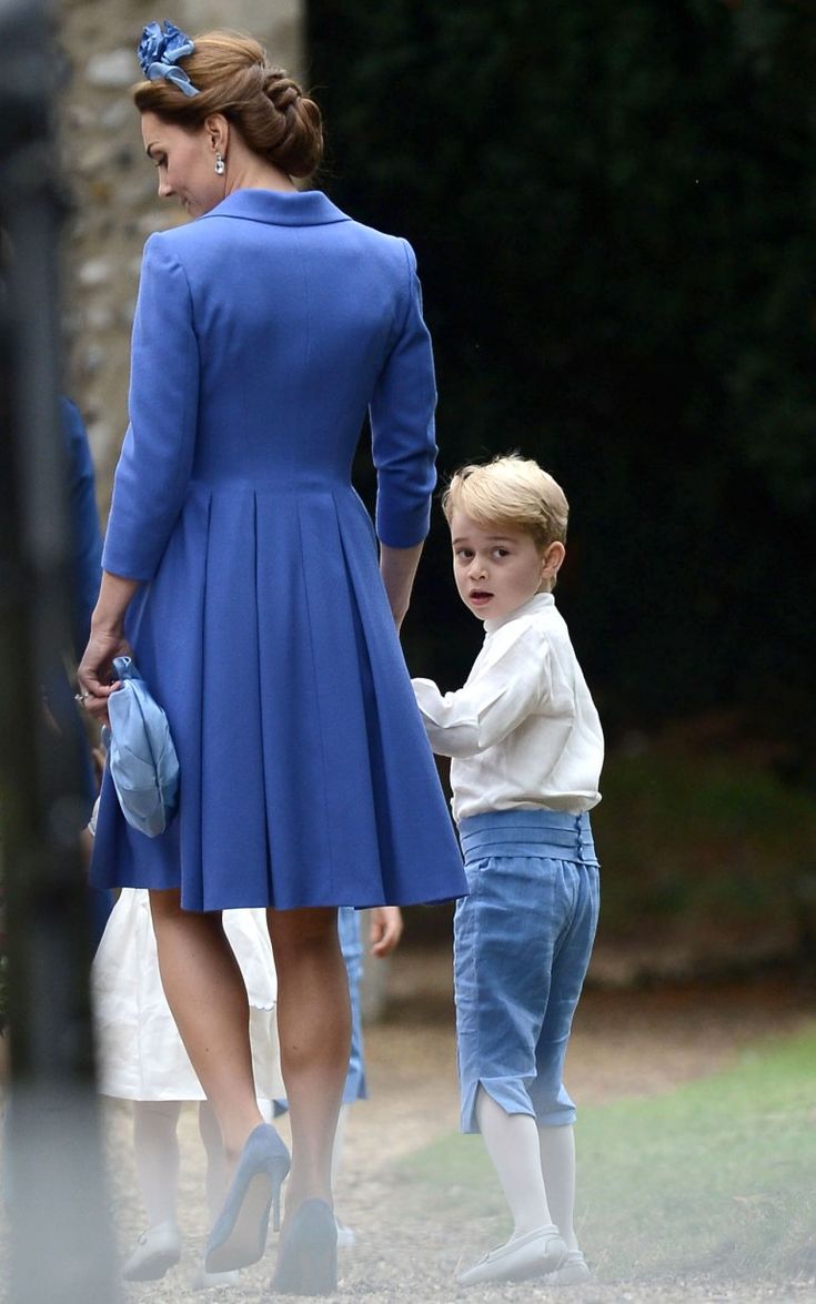 the young boy is walking next to his mother in blue dress and white shoes with her hand on her hip