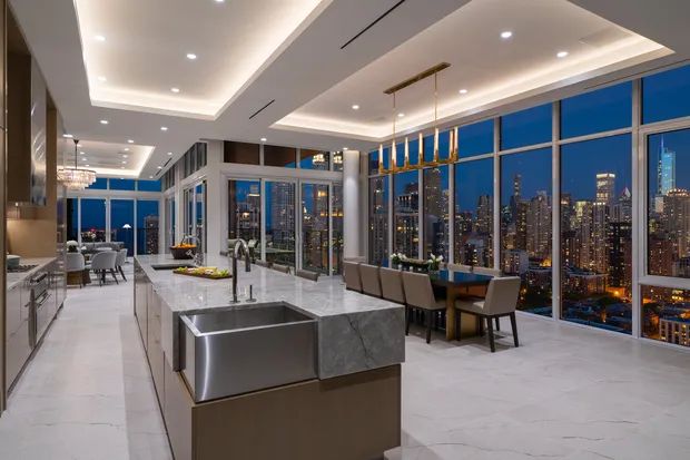 a large kitchen with an island in front of the city skyline at night time, and lots of windows