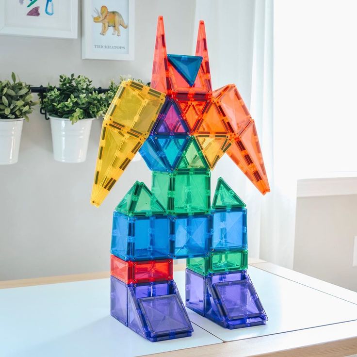 a colorful sculpture made out of plastic blocks on top of a white table next to a potted plant