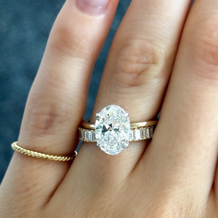 a woman's hand with a diamond ring on top of her finger and the other hand holding an engagement ring