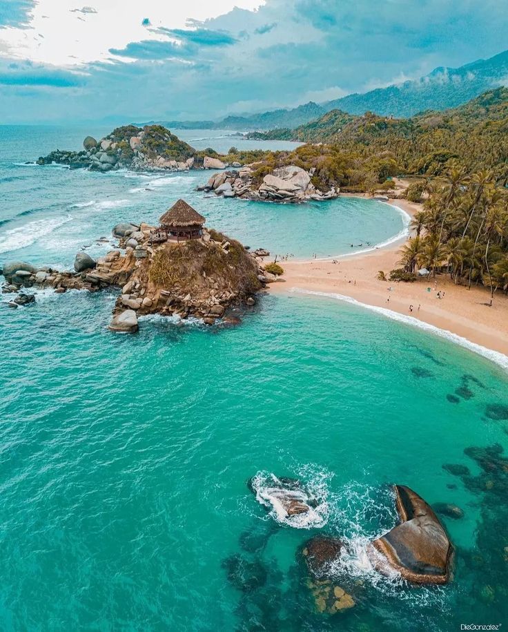 an aerial view of the beach and ocean with people swimming in it, surrounded by trees