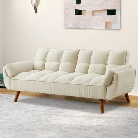 a white couch sitting on top of a wooden floor next to a wall mounted painting