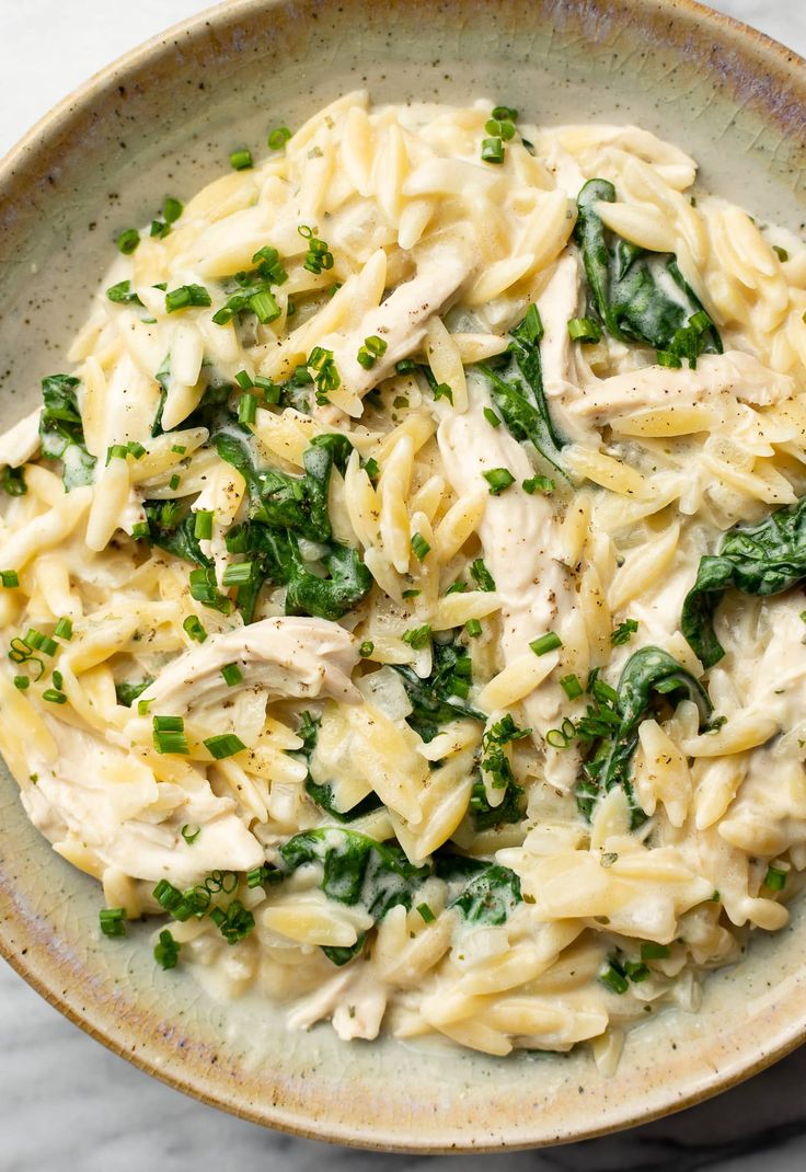 a bowl filled with pasta and spinach on top of a marble countertop next to a fork