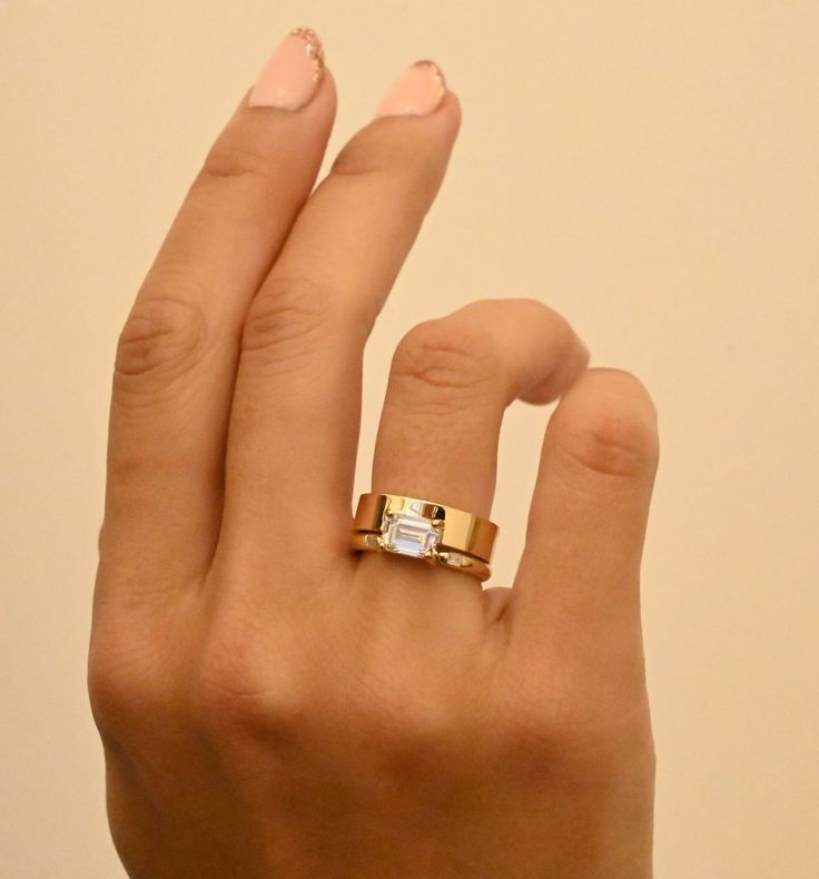 a woman's hand wearing a gold ring with a diamond in the middle and two diamonds on each band