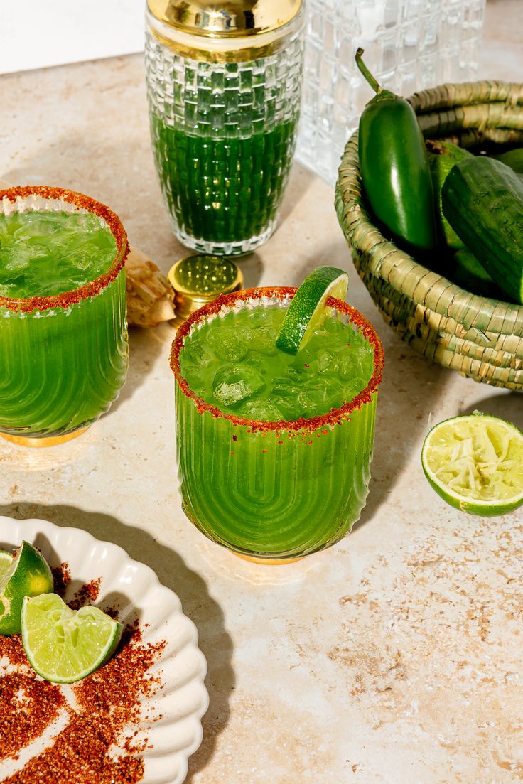 two glasses filled with green liquid next to some limes