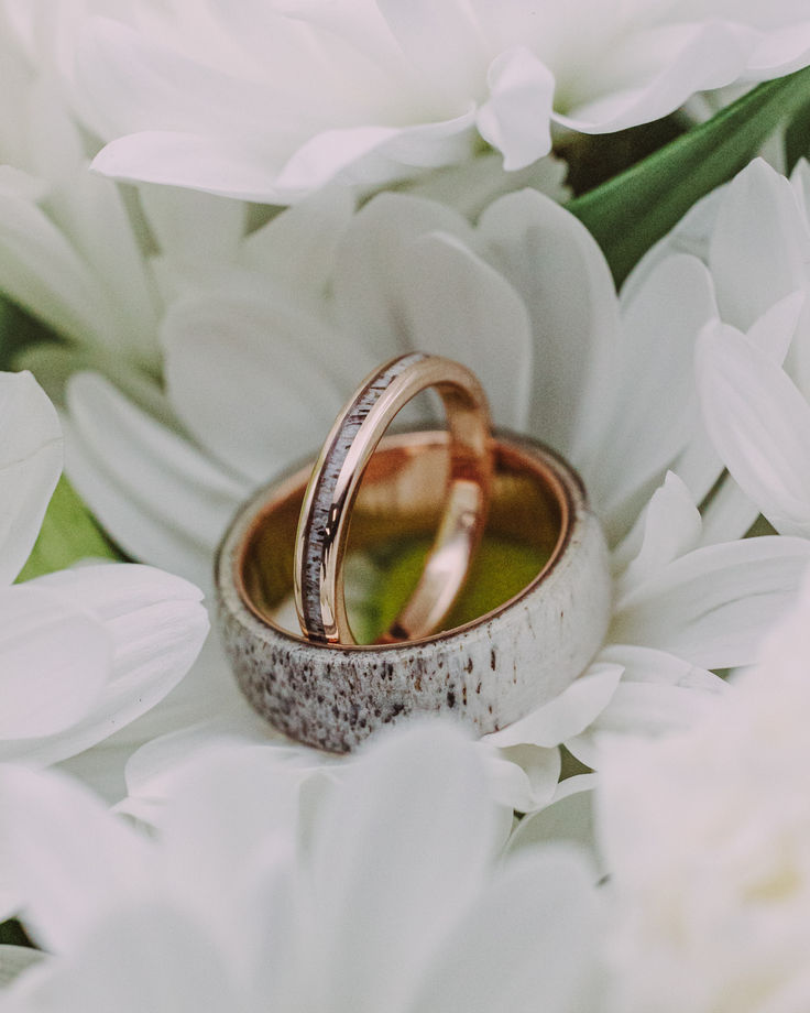 A matching antler wedding ring set from Staghead Designs sits in the petals of a flower. This set features our "Haven" design wedding band with a 14K rose gold base & elk antler overlay. It is paired with our "Eterna" narrow 14K rose gold band with elk antler inlay. Antler Wedding Ring, Whiskey Barrel Wedding Ring, Antler Wedding Rings, Matching Wedding Ring Sets, Matching Wedding Ring, Antler Wedding Band, Antler Wedding, Wood Wedding Ring, Handcrafted Engagement Ring