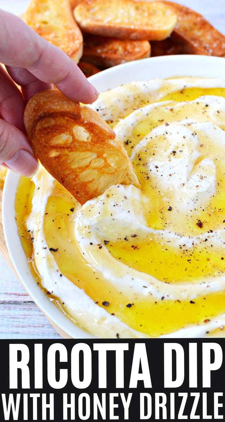 a hand dipping some bread into a bowl of dip with honey drizzled on top