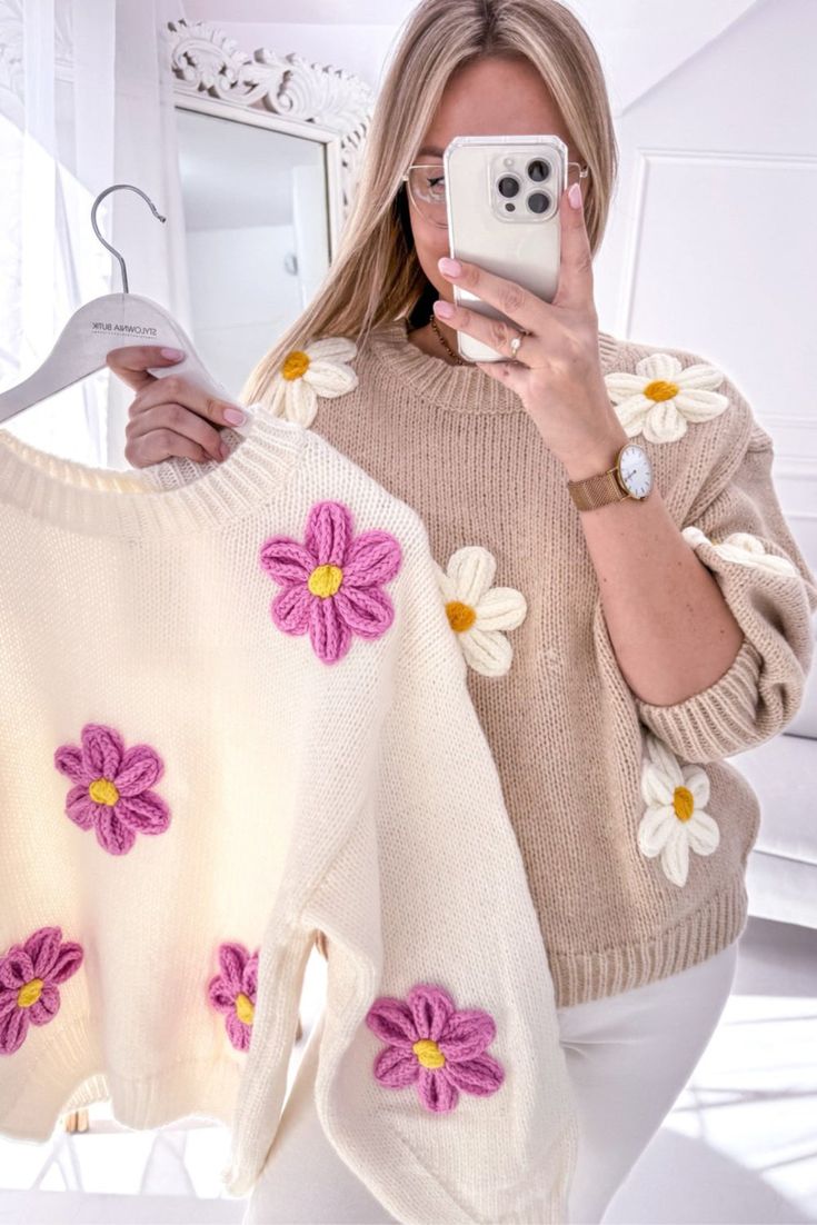 a woman taking a selfie in front of a sweater with flowers on the back