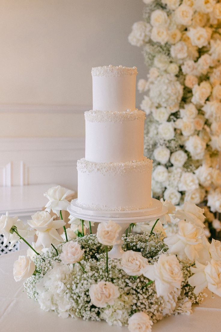 a white wedding cake sitting on top of a table covered in flowers and greenery