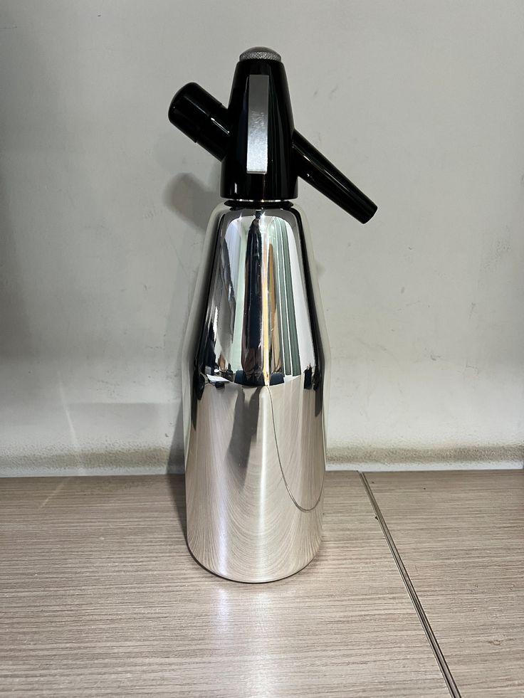 a silver coffee pot sitting on top of a wooden floor next to a white wall