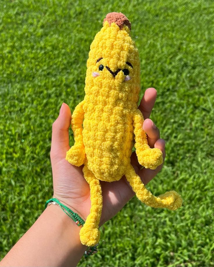 a hand holding a yellow crocheted stuffed animal in the middle of green grass