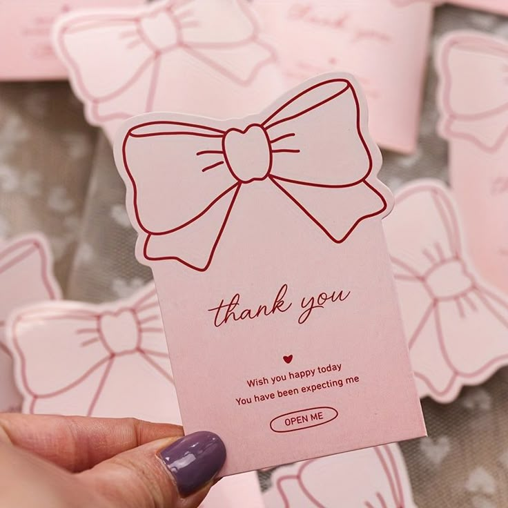 a person holding up a pink card with a bow on it that says thank you