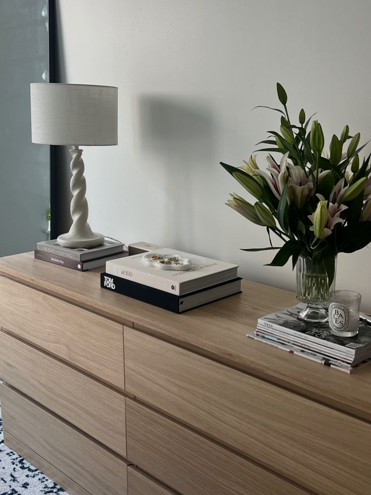 a vase filled with flowers sitting on top of a wooden dresser next to a lamp