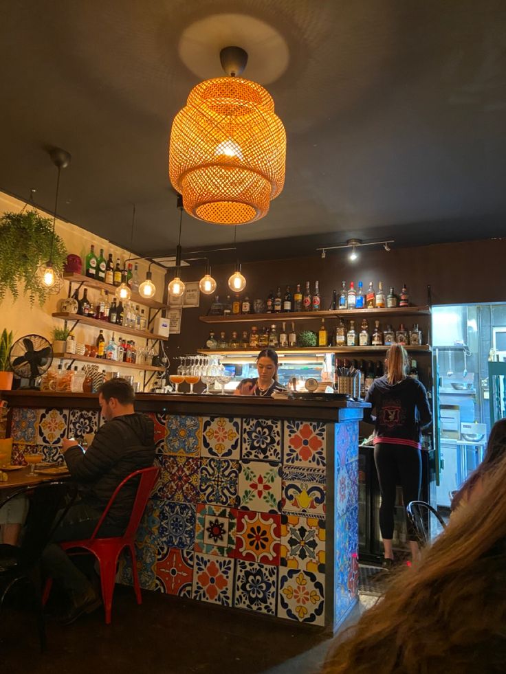 people are sitting at the bar in front of the wall with colorful tiles on it