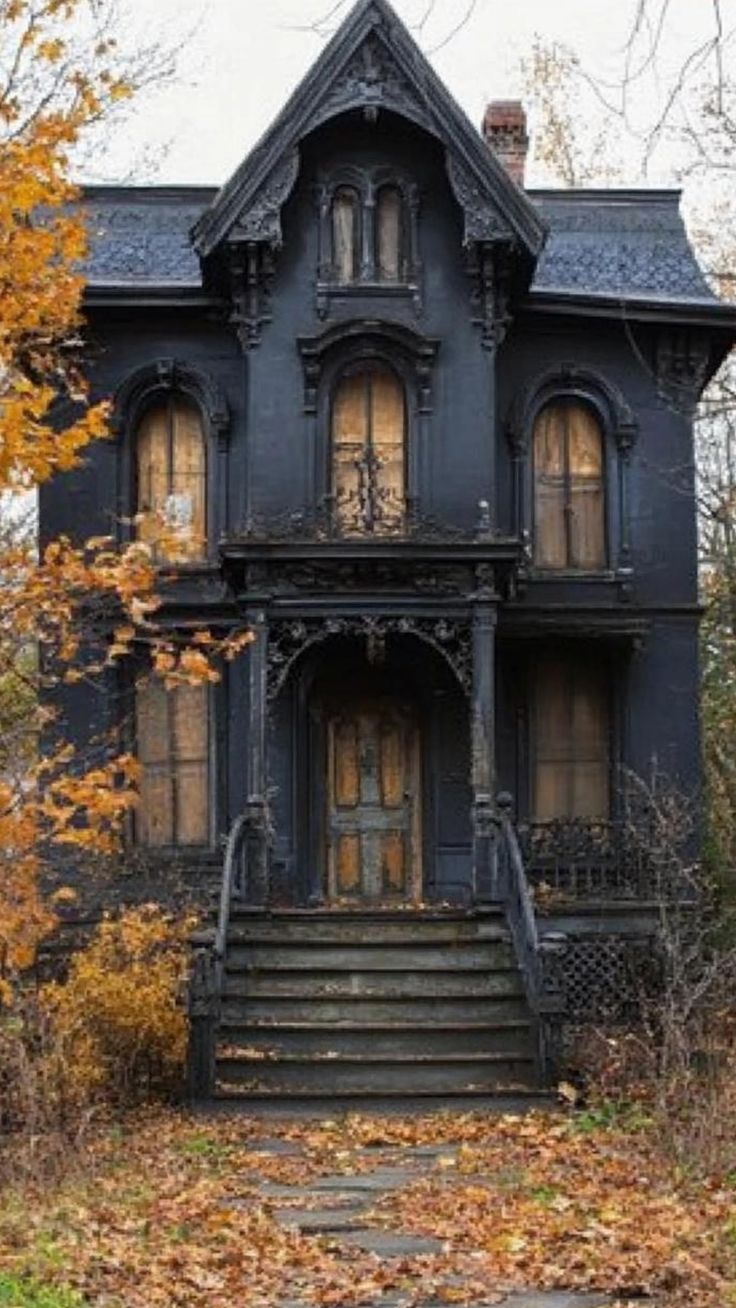 an old black house in the fall with leaves on the ground and stairs leading up to it