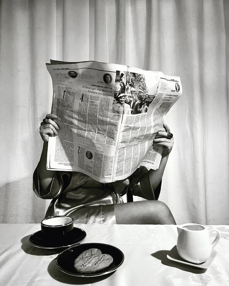 a woman sitting at a table reading a newspaper