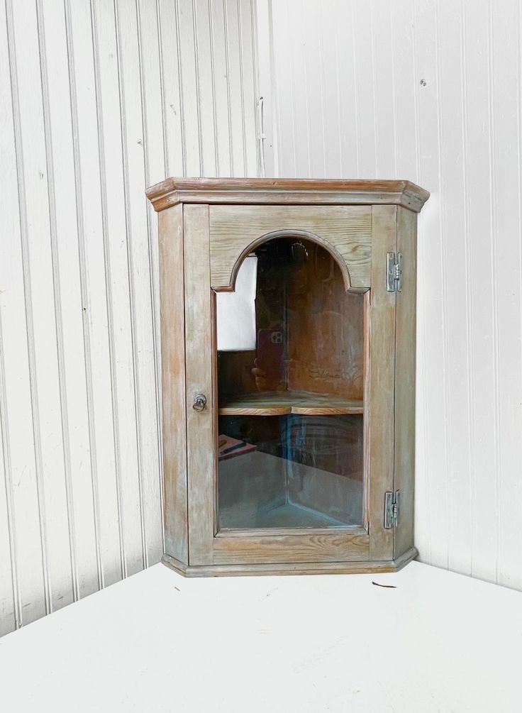 an old wooden cabinet with glass doors on the front and bottom, against a white wall