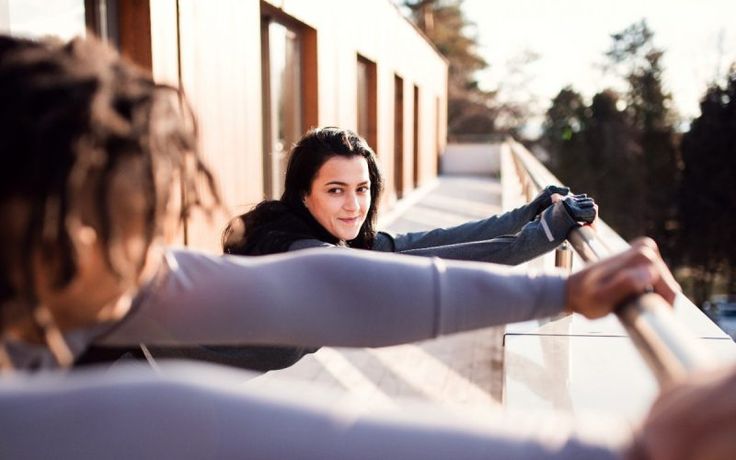 two women standing on the side of a building with their arms around each other as they look at something