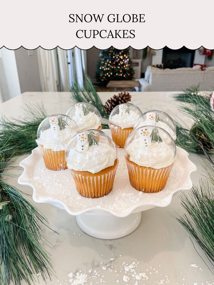 some cupcakes are sitting on a white platter with pine branches and snow globe ornaments