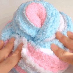 two hands are holding onto a small knitted object in blue, pink and white