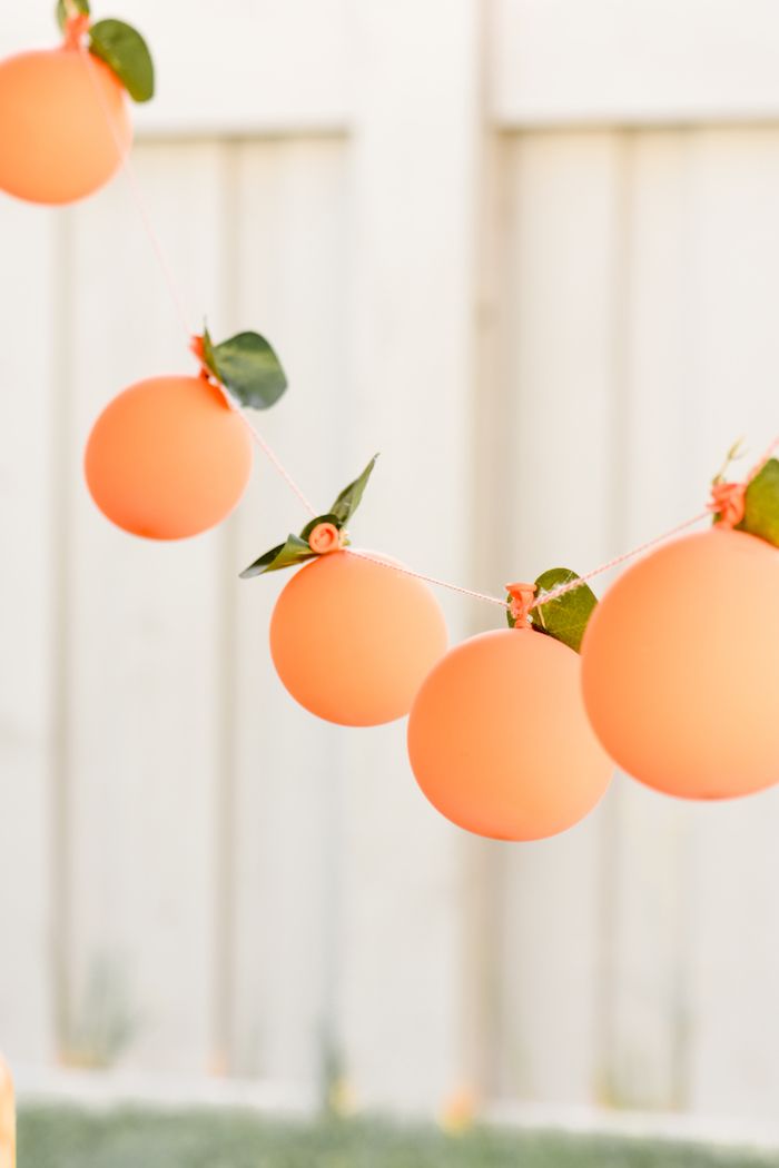 some oranges are hanging from a string with green leaves on them in front of a white fence