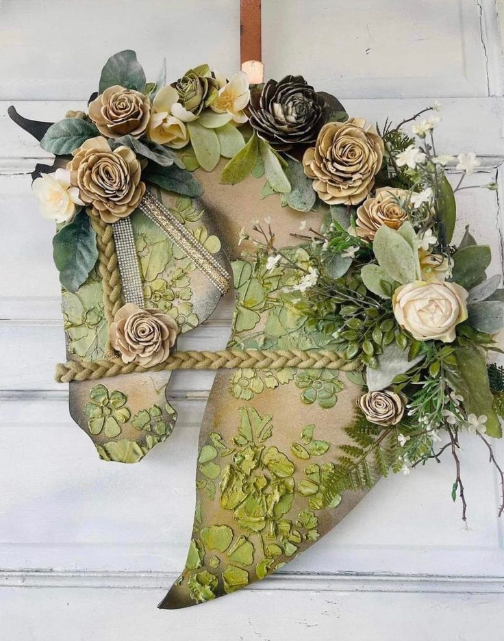 a green and white wreath with flowers hanging from the side of a door on a wooden hanger