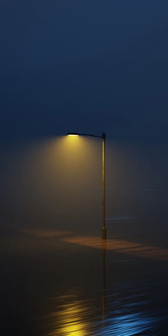 a street light sitting on top of a foggy beach next to the ocean at night