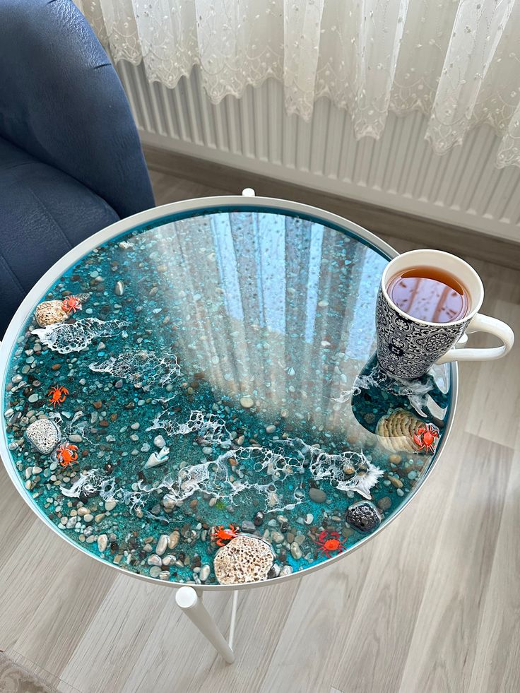 a glass table topped with a cup of tea and seashells on top of it