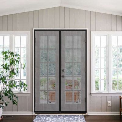 a living room with two windows and a rug in front of the door that is open