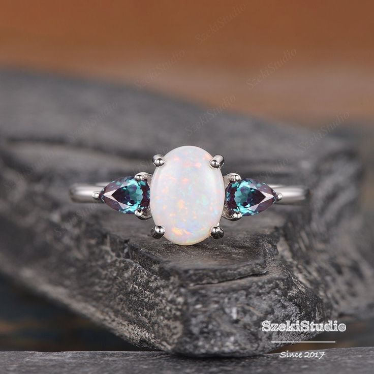 "Opal And Alexandrite Ring Oval Cut Cabochon Natural Opal Engagement Ring Three Stone Ring Pear Cut Lab Alexandrite Wedding Birthstone Ring ITEM INFORMATION Metal Type - Solid 14k Rose Gold Band Width - (approx. 1.5mm) Center Stone - 6*8mm Natural opal or Lab Opal, Oval Cut Side Stone - Lab Alexandrite Weight - 3*5mm Clarity - VVS Color - D-E-F **Stone Replacement** Available with any other gemstones, please feel free to contact me for a quote. **Metal Type** Available in 14K or 18K yellow gold, white gold, and rose gold. Please select from the drop down menu. **Production Time& Rush Order** Our standard production time is 3-4 weeks from time of purchase. I am very happy to provide rush order service, the price is $60, the Process time would be 10-15 business days instead of 3-4 weeks. Her Three Stone Oval Cabochon Rings For Anniversary, Oval Cabochon Gemstones For Weddings, Oval Multi-stone Opal Ring For Anniversary, Oval Opal Ring With Accent Stones, Round Cabochon Gemstones For Wedding, Wedding Birthstone Ring With Cabochon Cut, Cabochon Gemstones For Wedding, Oval Three Stone Opal Ring Fine Jewelry, Oval Three Stone Opal Promise Ring